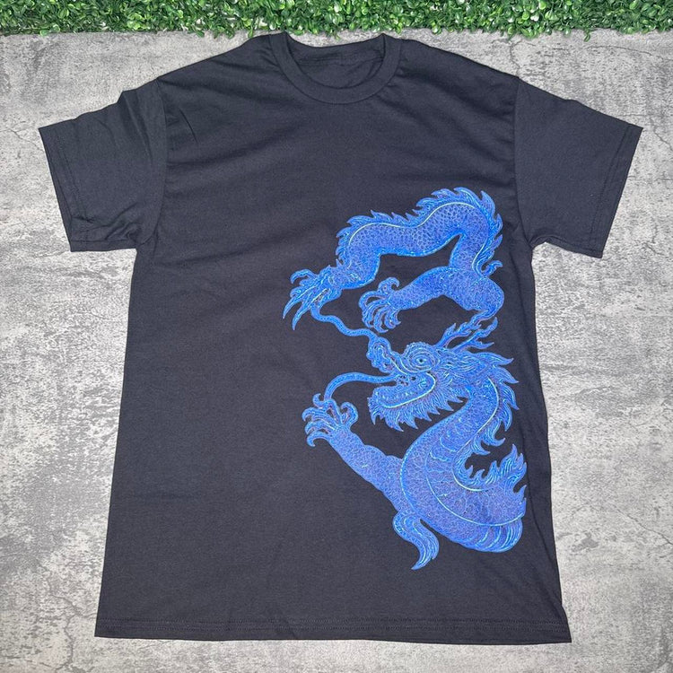 Black tee with intricate blue dragon artwork on concrete with grass above