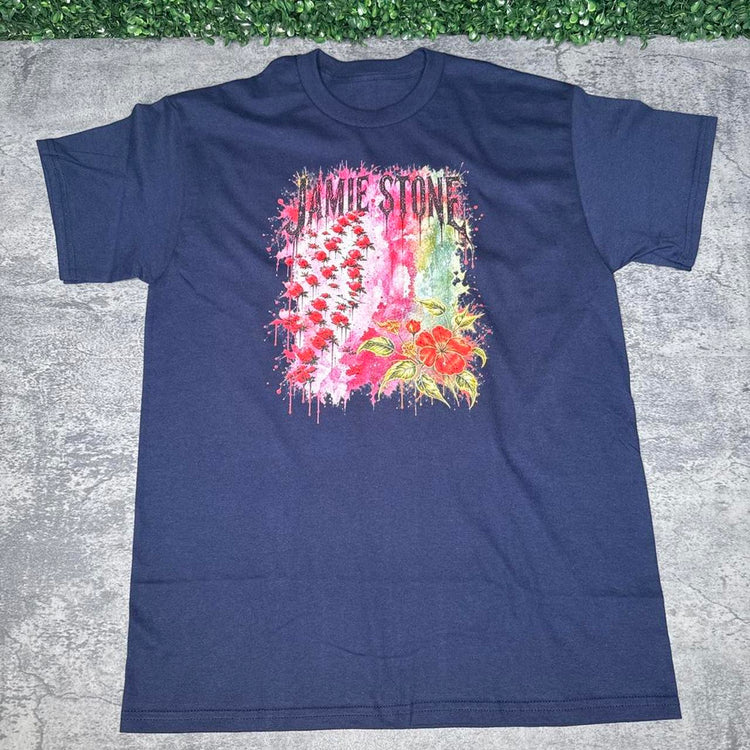 Navy blue Jamie Stone floral tee flat lay on gray concrete with green grass above