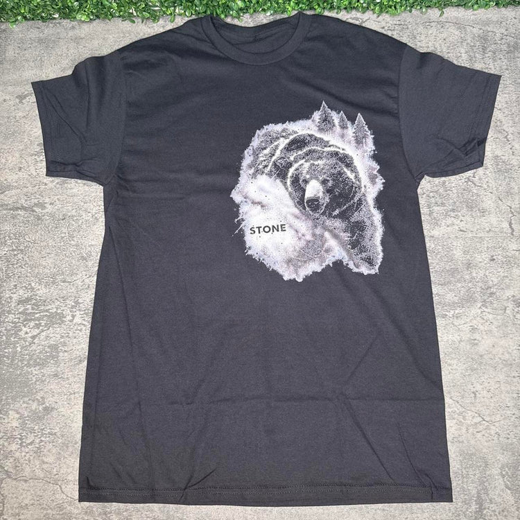 Black STONE forest bear tee flat lay on concrete with grass above