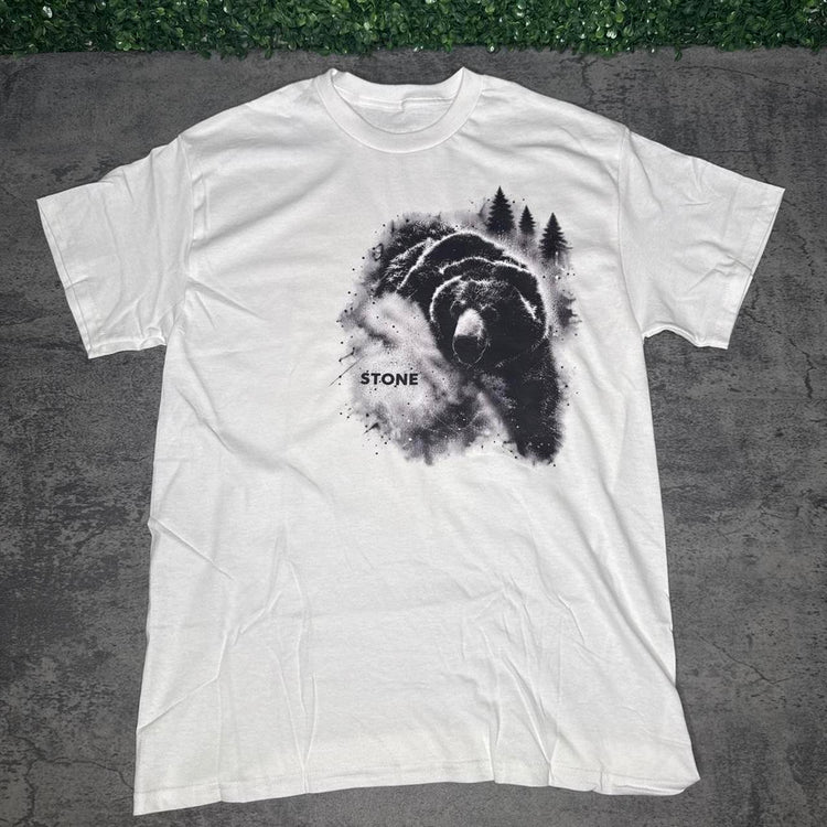 White STONE tee with black bear and pine tree artwork on concrete with grass above