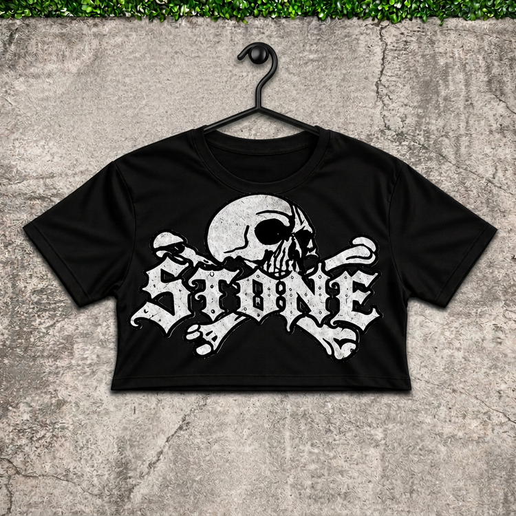 Black STONE skull women's crop top on a black hanger against concrete with green grass above