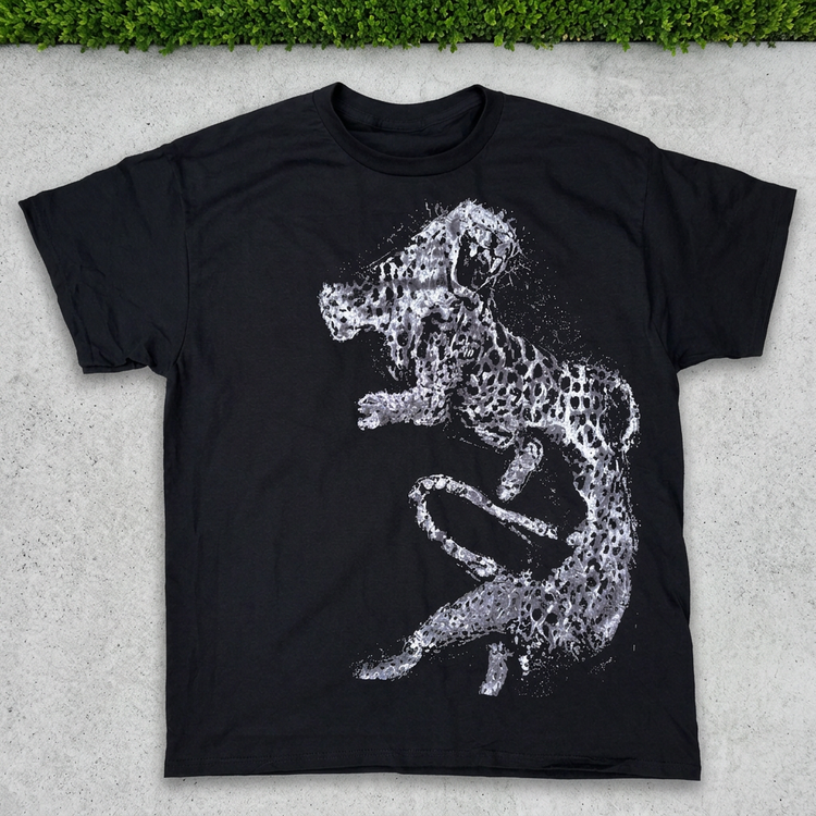 Black silver leaping cheetah tee flat lay on concrete with grass above