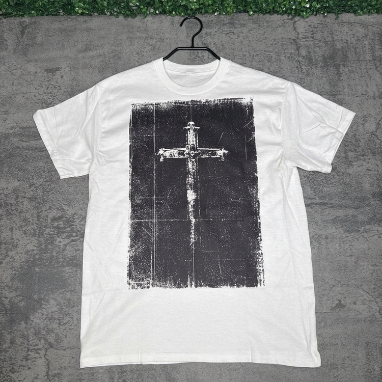 White distressed cross tee on a hanger against gray concrete with green grass above