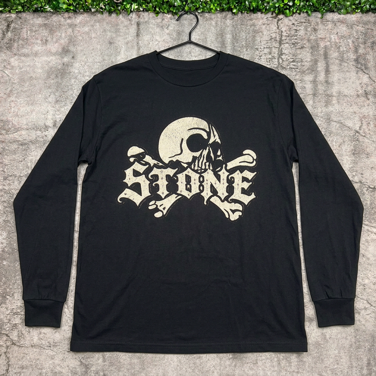 STONE skull long-sleeve tee on a hanger against concrete with grass above