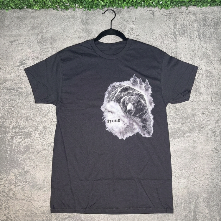 Black STONE forest bear tee on a hanger against gray concrete with green grass above