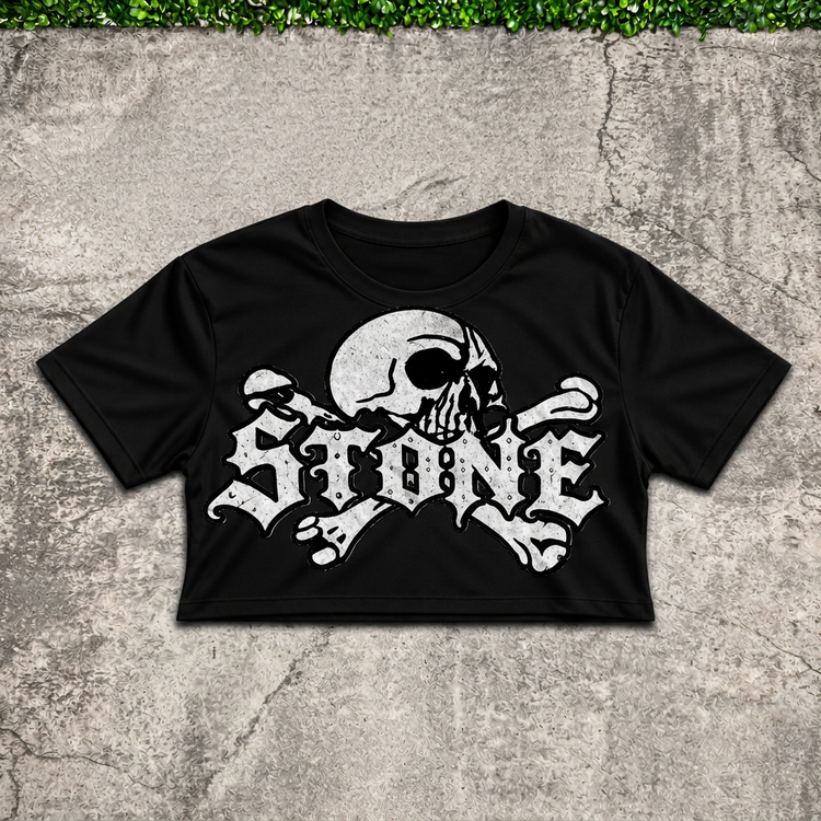Black STONE skull women's crop top flat lay on concrete with green grass above