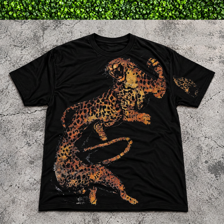 Black leaping cheetah tee flat lay on gray concrete with thin green grass strip